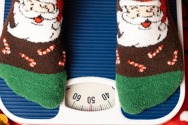 stock image A woman in Christmas socks stands on the scales, weighs herself after gluttony during the holidays.