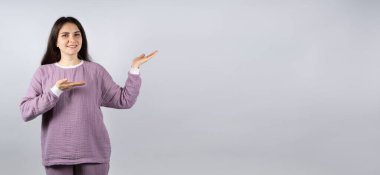 Lavanta rengi müslin pijamalı güzel esmer kadın mesaj için ellerini mekâna gösteriyor..