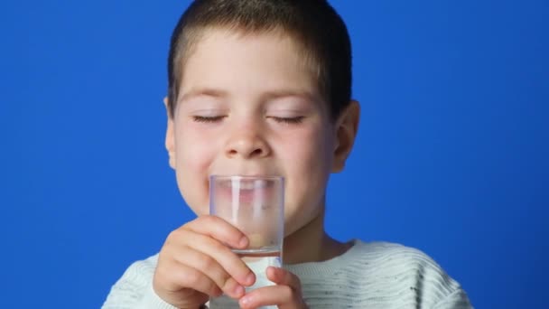 Щасливий Річний Хлопчик Тримає Склянку Води Роті Посміхається Синьому Фоні — стокове відео