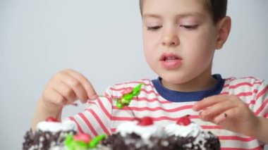 Yakışıklı 5 yaşındaki bir çocuk beyaz arka plandaki pastadan lezzetli bir krema yiyor..