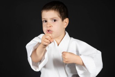 Küçük bir çocuk dövüş sanatları yapıyor. Kimono karate dersleri alıyor. Siyah bir arka planda..