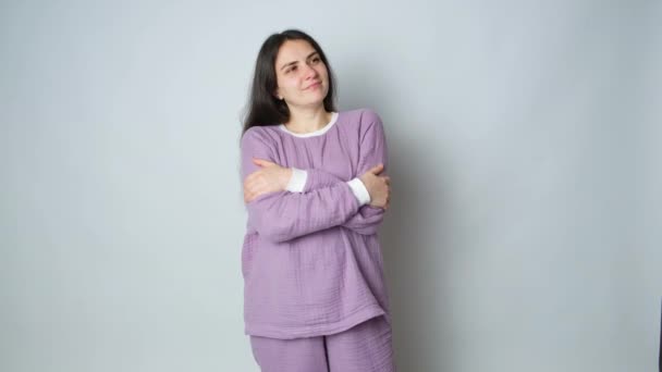 紫の暖かいムスリンパジャマのブルネットの女性は自分自身を抱き 眠っている服の快適さを楽しむ — ストック動画