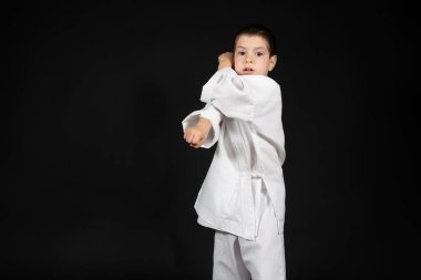Küçük bir çocuk dövüş sanatları yapıyor. Kimono karate dersleri alıyor. Siyah bir arka planda..