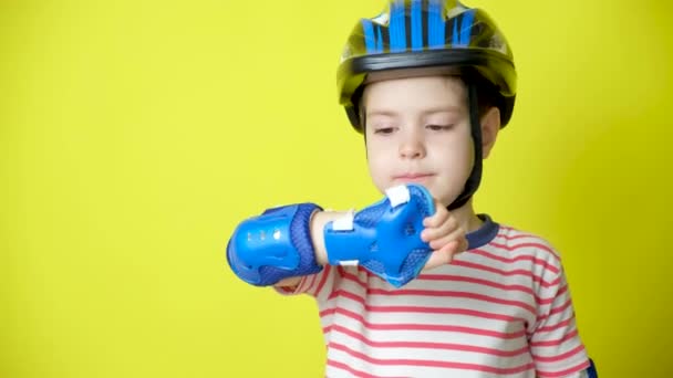 黄色の背景に保護ヘルメット 肘パッドと手袋の小さな男の子 自転車 スケートボード ローラースケートに乗るときの保護 — ストック動画