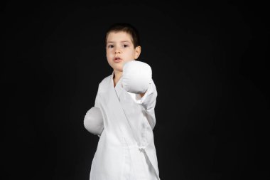 Küçük bir çocuk dövüş sanatları öğreniyor, kimono ve boks eldivenleriyle karate yapıyor.