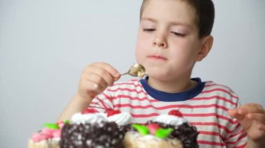 Anaokulu 5 yaşında bir çocuk kaşıkla pasta yiyor ve beyaz bir arka planı yalıyor..