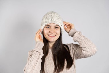 Kış şapkalı mutlu bir esmer kadın ve örgü ören süveter beyaz bir arka planda gülümsüyor.
