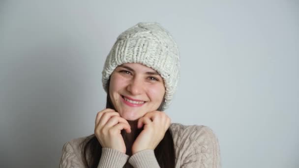 冬の帽子をかぶった幸せなブルネットの女性とニットセーターは白い背景で笑顔 — ストック動画