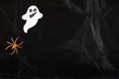 Yüzü gülümseyen neşeli beyaz bir hayalet ve siyah bir arka planda uçan bir örümcek ve bir ağ, mesaj için bir yer.