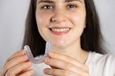 A woman holds dental mouthguard, splint for the treatment of dysfunction of the temporomandibular joints, bruxism, malocclusion, to relax the muscles of the jaw clipart