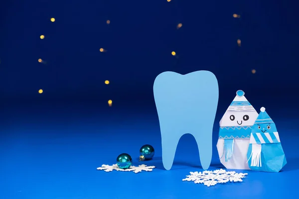 Christmas dentistry - big tooth, snowmen and balls on a blue background, garlands of bokeh