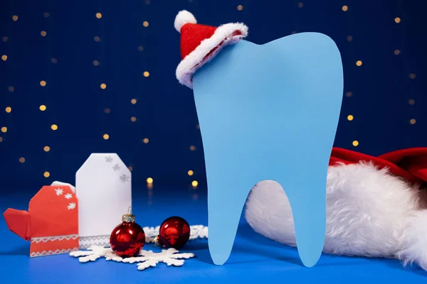 Christmas dentistry - tooth with red santa claus hat, mittens on a blue background