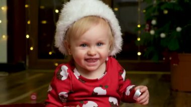 Noel kıyafetleri içinde bir yaşındaki güzel bir kız Noel Baba 'nın şapkasını çıkarır ve kameraya bakıp gülümser.