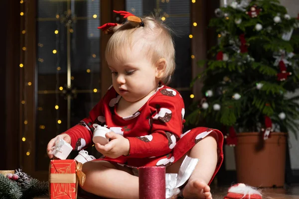 Beautiful little one-year-old girl with blonde hair playing Christmas gifts. Bokeh garlands. Children and new years eve.