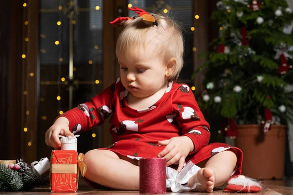 Beautiful little one-year-old girl with blonde hair playing Christmas gifts. Bokeh garlands. Children and new years eve.