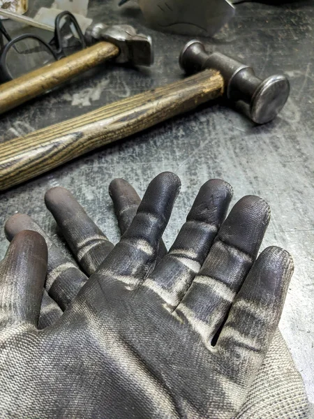 Black blacksmith work gloves against a sledgehammer background. Hard men\'s work as a blacksmith