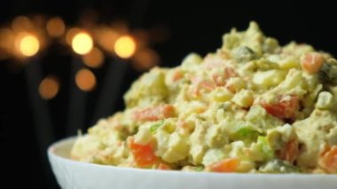 Olivier russian salad - a classic recipe with mayonnaise, an incredible taste, on a black background, with bokeh of sparklers for christmas and new year.