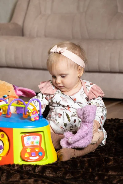 A happy one-and-a-half-year-old girl plays with toys sitting on the floor