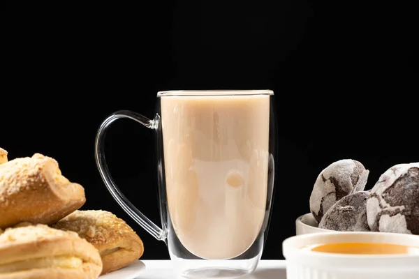 Tea with milk in a glass cup with a double bottom and cookies with gingerbread on a black background.