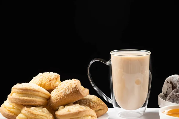 Tea with milk in a glass cup with a double bottom and cakes on a black background, place for text.