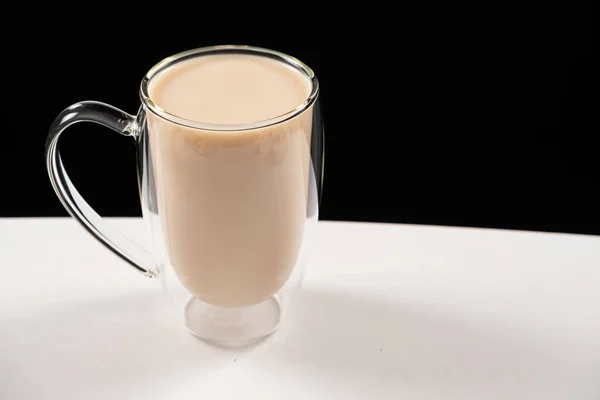 Tea with milk in a glass cup with a double bottom on a white and black background.