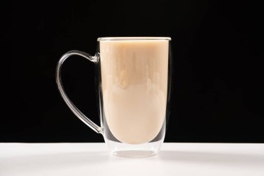 Tea with milk in a glass cup with a double bottom on a white and black background.