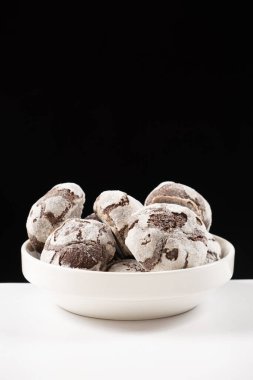 Chocolate chip cookies with cocoa and powdered sugar on a plate on a black background