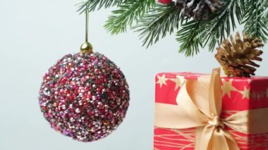 A shiny pink ball spins on a snow-covered Christmas tree, a red gift with a ribbon