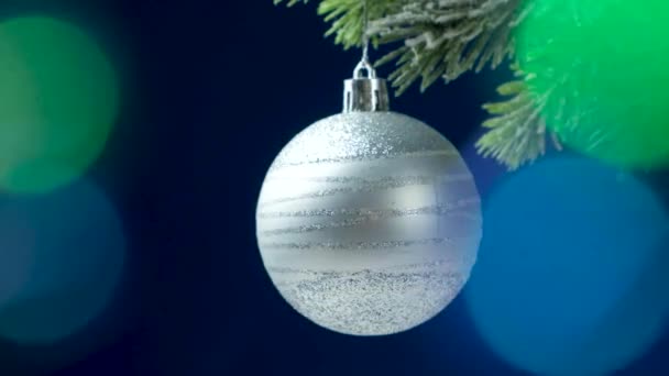 一颗闪亮的灰色球落在圣诞树上深蓝色背景的花环灯 — 图库视频影像