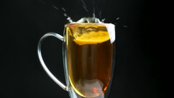 柠檬落在茶里 倒入一个黑色背景的杯子里 溅着茶 — 图库视频影像