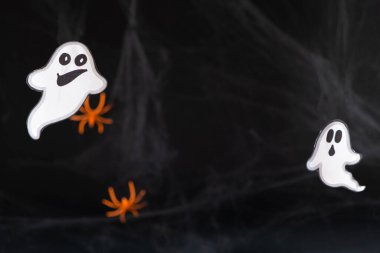 Örümcek ağları ve örümceklerle siyah arka planda kağıttan yapılmış iki neşeli hayalet. Ortasında metin için boşluk ile.