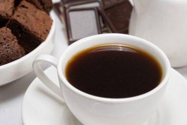 Coffee in a cup close-up, chocolate cake and pieces of chocolate on a white background.