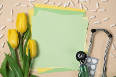 Spring and medicine - yellow tulips and stethoscope with space for text on a light green background