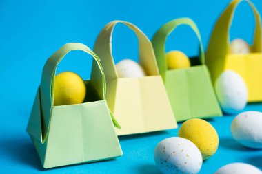 Origami paper baskets and painted quail eggs on a blue background, happy Easter.