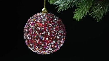 Karla kaplı bir Noel ağacında dönen parlak pembe bir top, siyah arka plan.