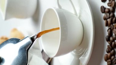 The process of pouring coffee from a geyser moka coffee maker into a white cup.