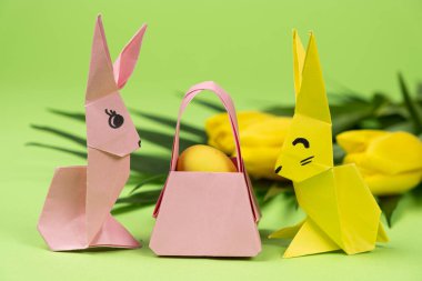 Easter origami - two paper bunnies and an egg, green background. Crafts for the holiday, do it yourself.