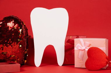 Valentine's Day in dentistry - a large white tooth, a heart and boxes of gifts on a red background, a place for text.