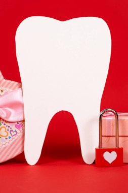 Valentine's Day in dentistry - a large white tooth, a heart and boxes of gifts on a red background, a place for text.
