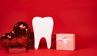 Valentine's Day in dentistry - a large white tooth, a heart and boxes of gifts on a red background, a place for text.