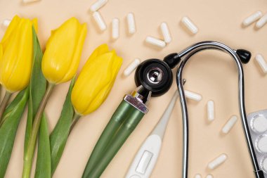 Holiday medicine - stethoscope, pills and flowers on a beige background.