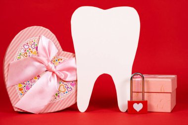 Valentine's Day in dentistry - a large white tooth, a heart and boxes of gifts on a red background, a place for text.