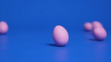 Pink chocolate Easter eggs roll across a blue background, knocking each other down