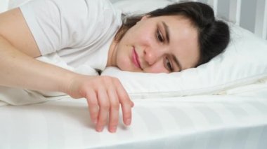 A brunette woman lies in bed and runs her hand over delicate soft bed linen, hugs a pillow