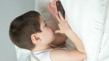 5 yaşında bir çocuk yatakta yatarken telefonuyla oyun oynuyor. Bir çocukta yatmadan önce yatma zamanı..