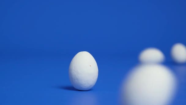 Λευκά Σοκολατένια Πασχαλινά Αυγά Κυλούν Ένα Μπλε Φόντο Χτυπώντας Ένα — Αρχείο Βίντεο