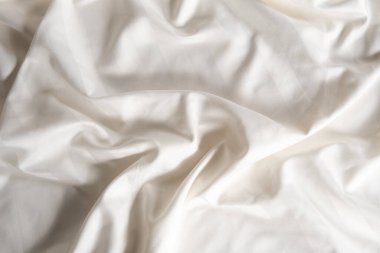 Satin crumpled fabric of light milky color, top view. Natural bed linen, sheets, abstract background of luxury fabric, wavy folds.