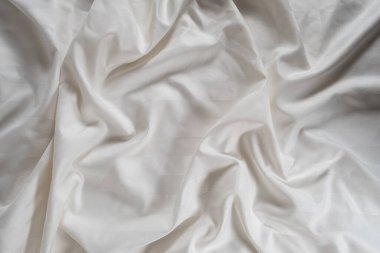 Satin crumpled fabric of light milky color, top view. Natural bed linen, sheets, abstract background of luxury fabric, wavy folds.