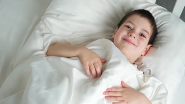 Handsome Year Old Boy Lies Bed Covered Blanket Smiles Childrens — Stok video