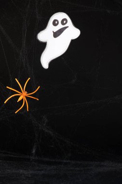 A cheerful white ghost with a face smiles and flies on a black background with a web and spider